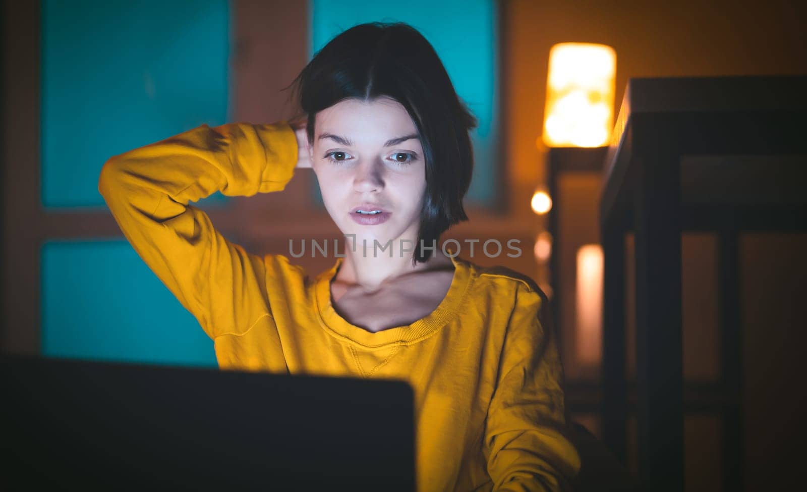 Portrait of beautiful caucasian girl uses laptop while sitting at home. In the evening creative woman works on a computer in her cozy living room. by africapink