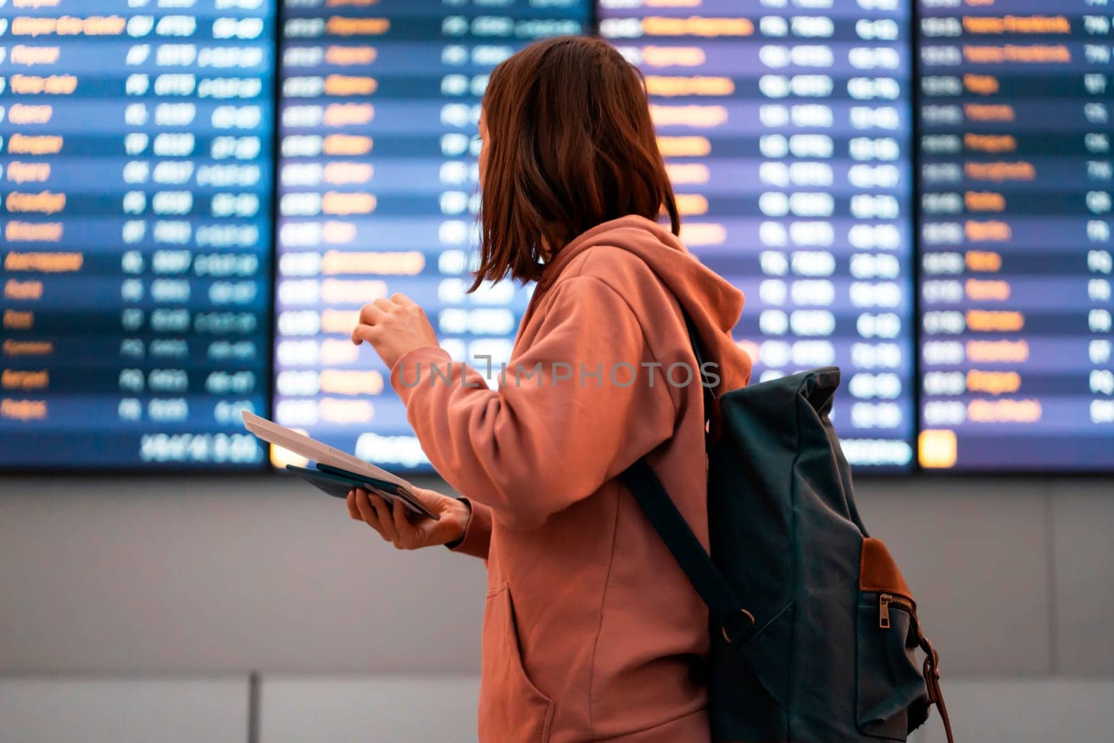 The girl goes on a flight in the airport, holds a passport and tickets in her hands, looks at the gate number in search of her plane, the woman goes on a trip with a backpack.
