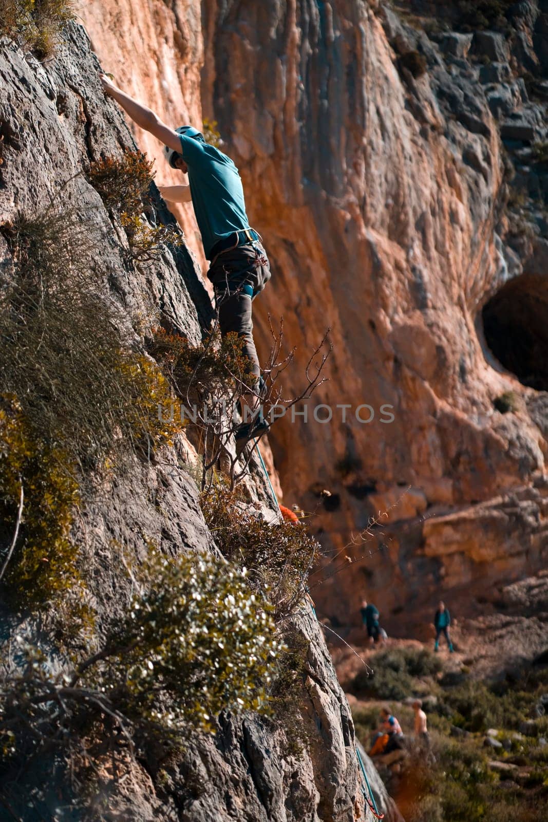 A young man is engaged in extreme sports, leads an active lifestyle, climbs a rock with climbing equipment in the sunny day against the background of Twin Caves, Leonidio, Arcadia, Greece.