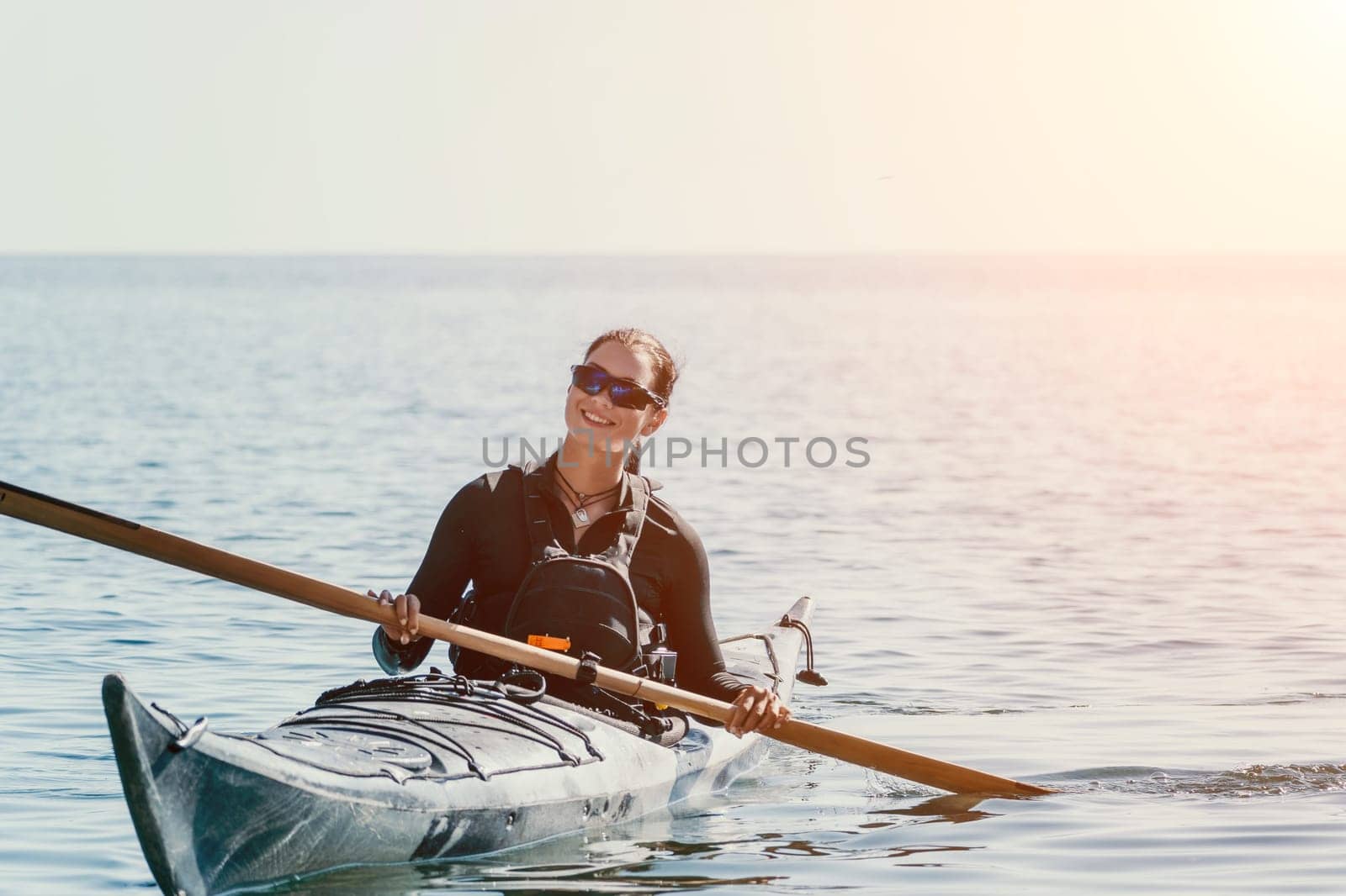 Happy smiling woman in kayak on ocean, paddling with wooden oar. Calm sea water and horizon in background