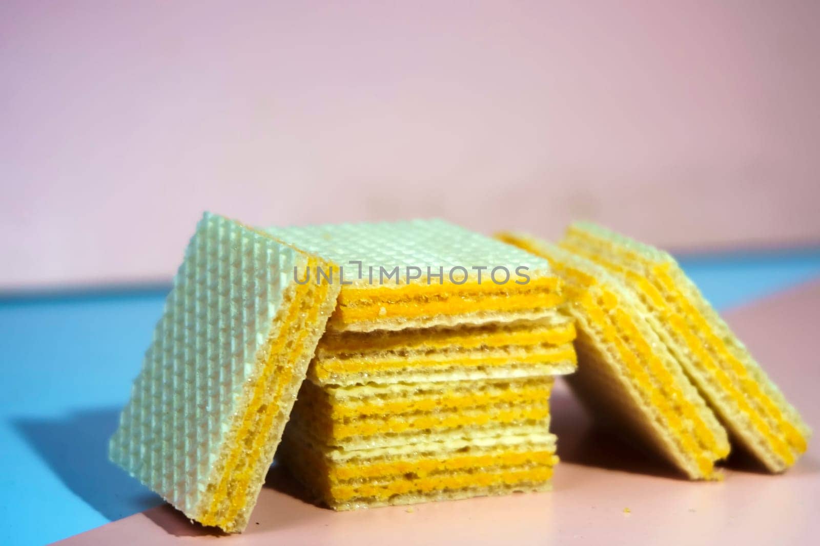 A pile of square, yellow wafers arranged on a blue and pink background. Copy space