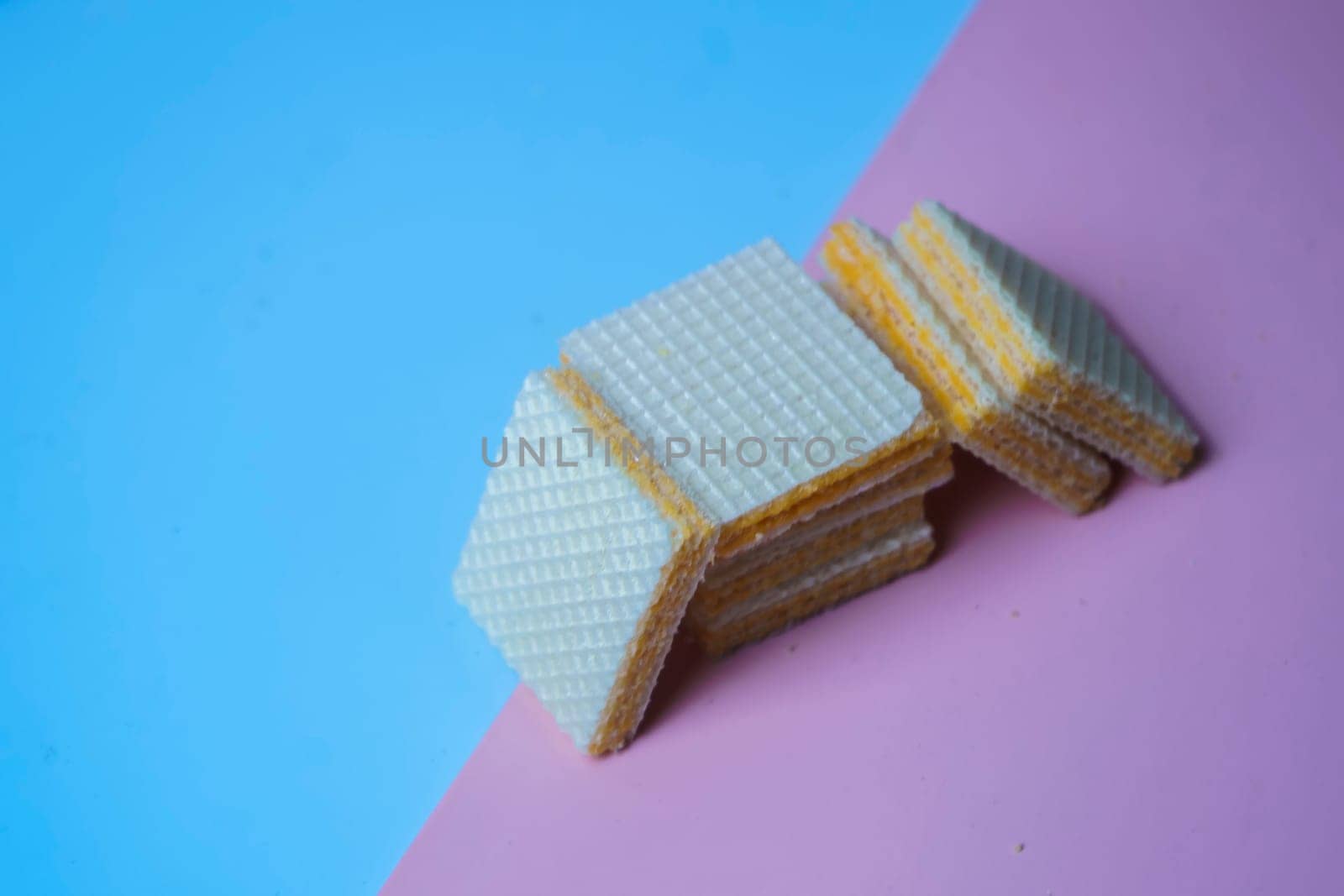 A pile of square, yellow wafers arranged on a blue and pink background. Copy space