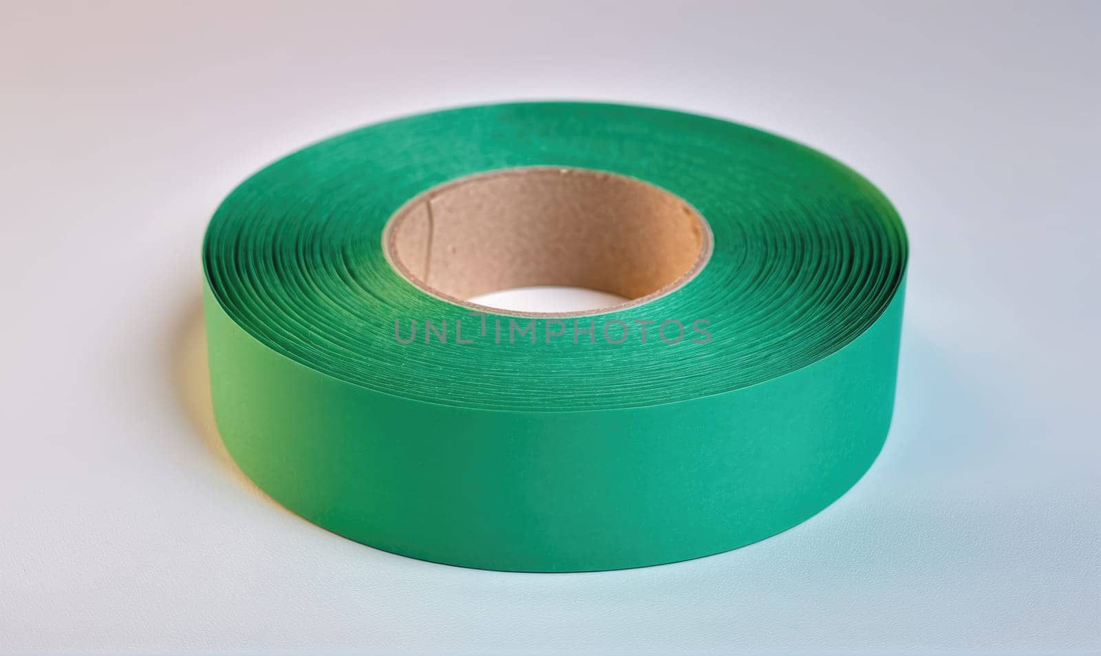 A roll of green tape is lying on a white background. The tape is wound around a cardboard core.
