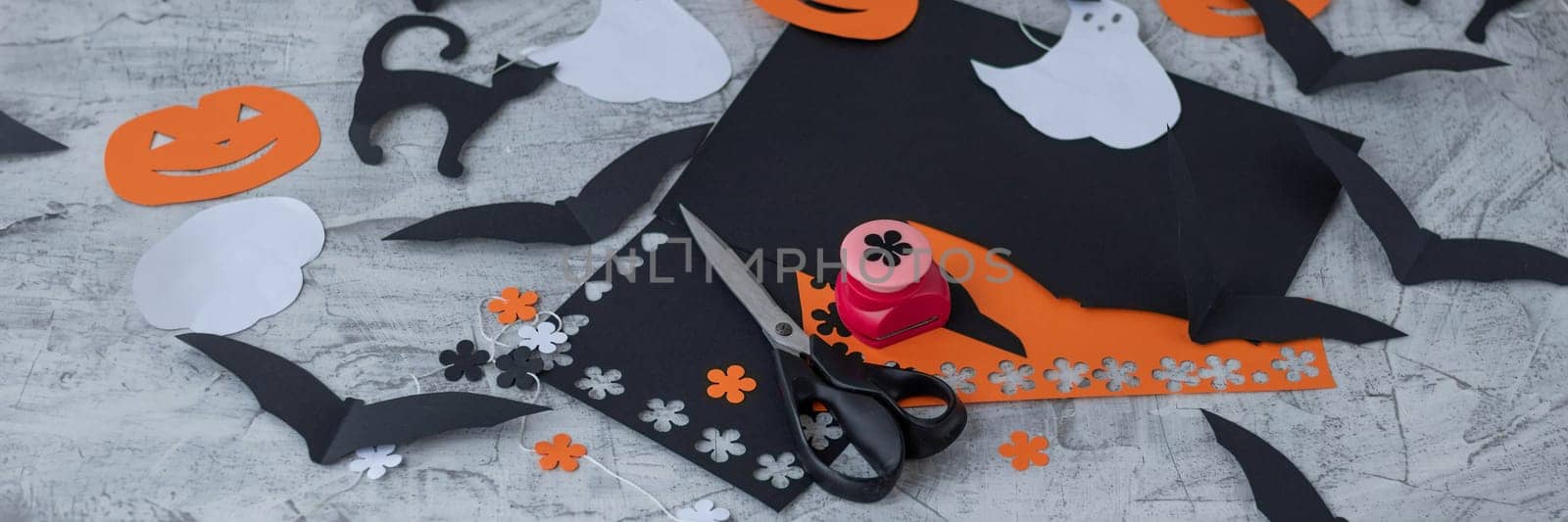 banner with paper decor for Halloween. carved orange pumpkin, jack-o'-lantern, white ghost, black cat. Preparation for the holiday, scissors and colored paper, paper garland. soft focus