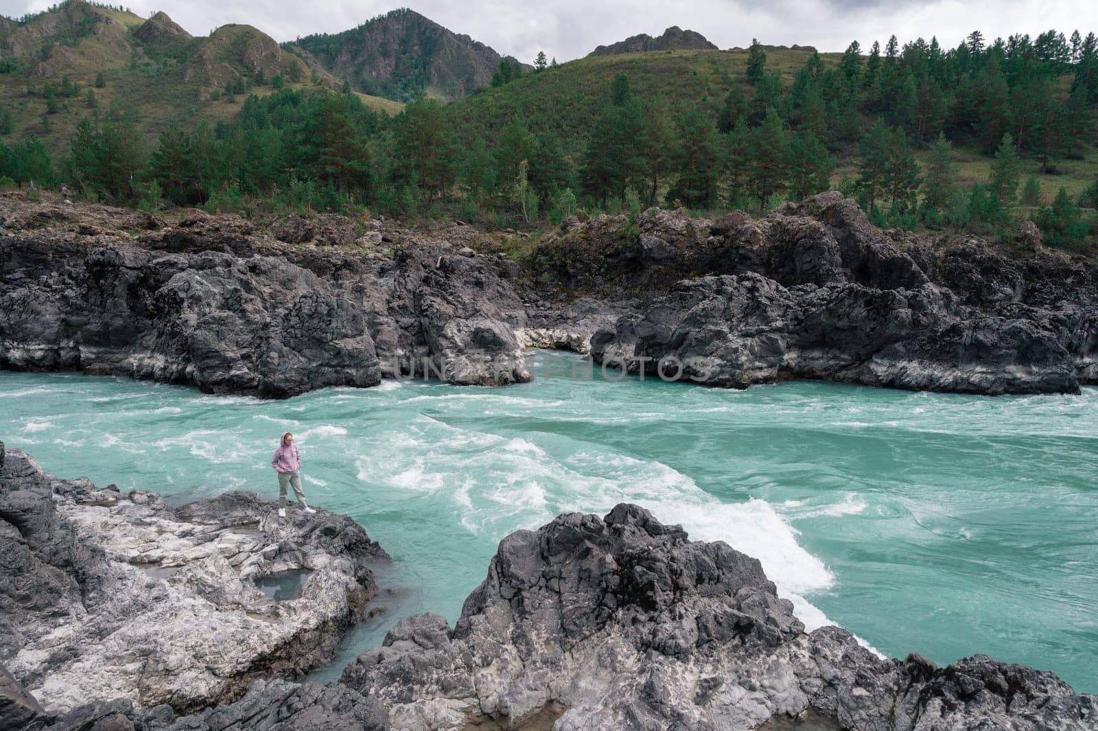 A solitary figure stands firmly on the rocks by a flowing, turquoise Katun river that is surrounded by lush greenery