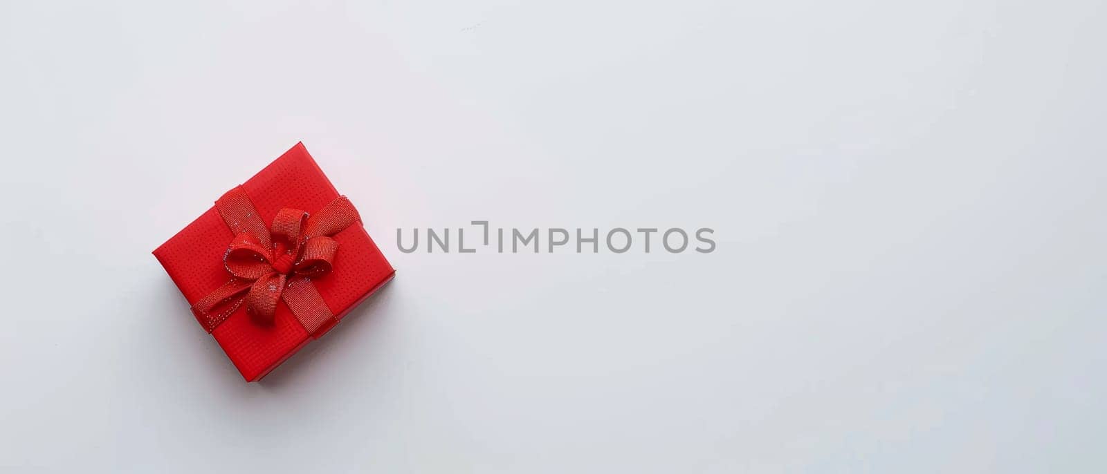 A minimalist red gift box with a neatly tied bow stands out on a pristine white background, symbolizing elegance and thoughtful giving. Its crisp presentation suggests a modern twist to gift-giving