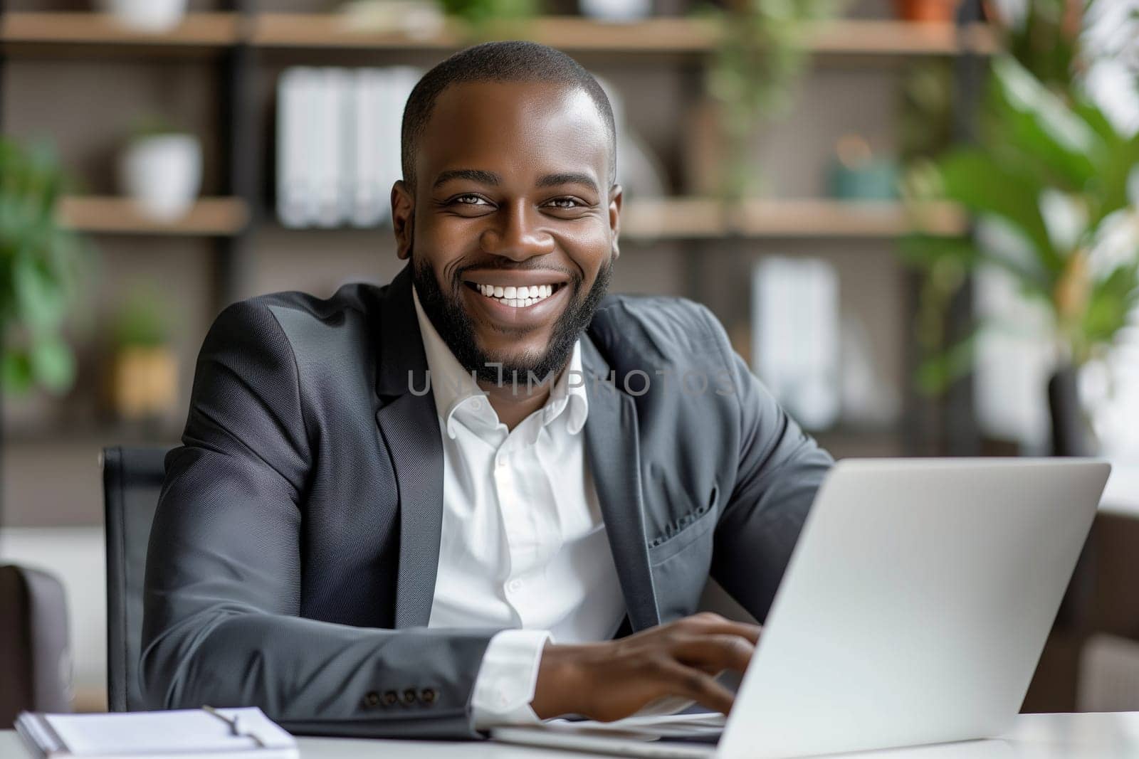 Happy successful African young businessman working on a laptop, smiling black male entrepreneur sitting in a cafe
