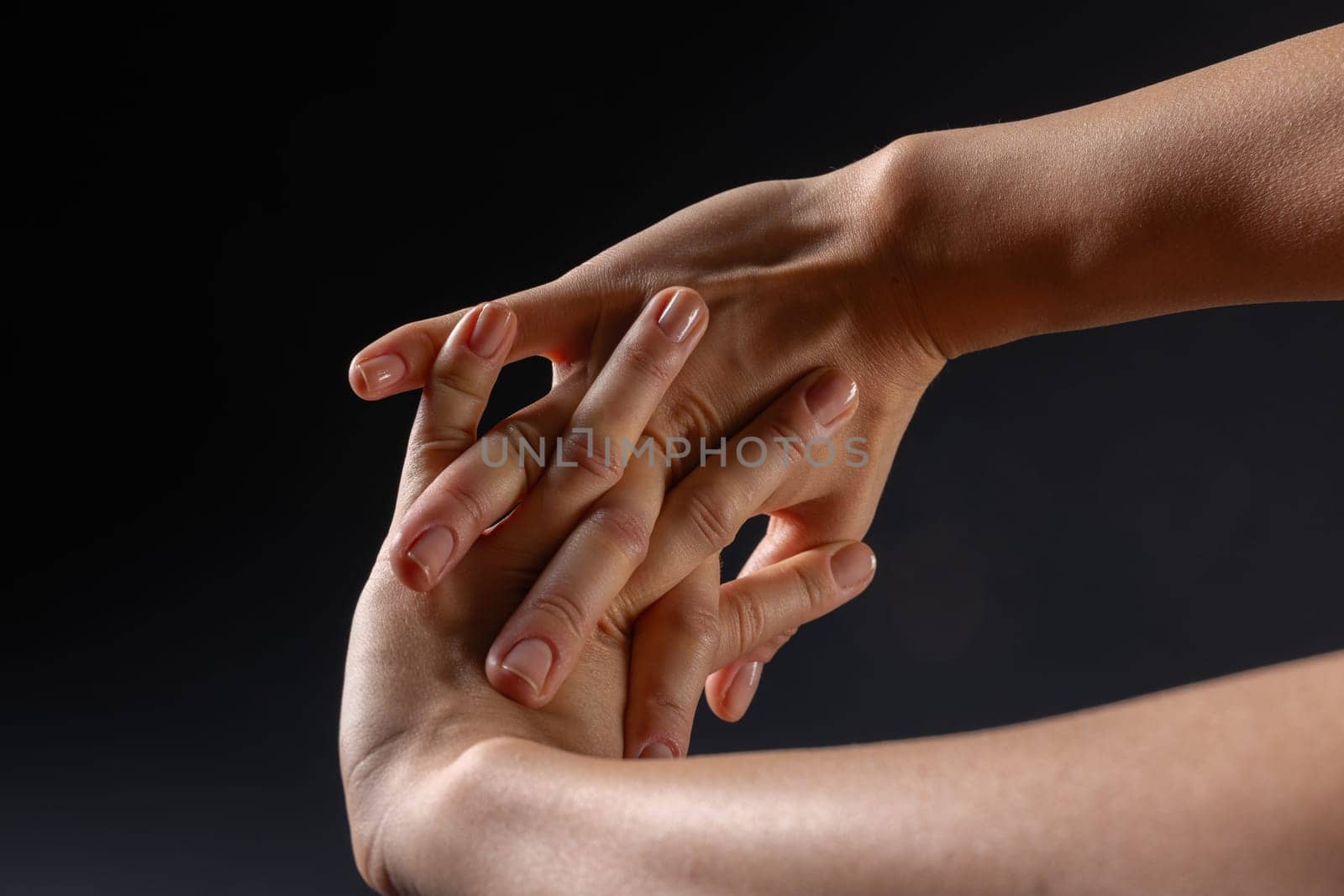 close up of female hands doing wrist stretching on dark background, concept of warm up and wrist fatigue