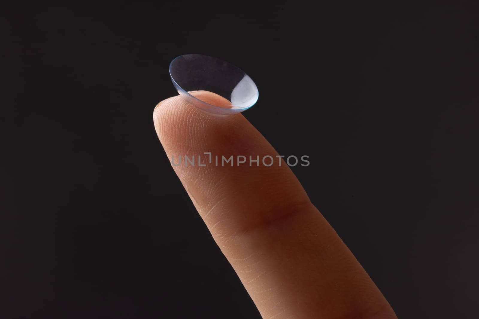 Close-up of finger holding contact lens, on grey background, concept of poor eyesight, astigmatism, myopia, hyperopia, treatment of deteriorating vision