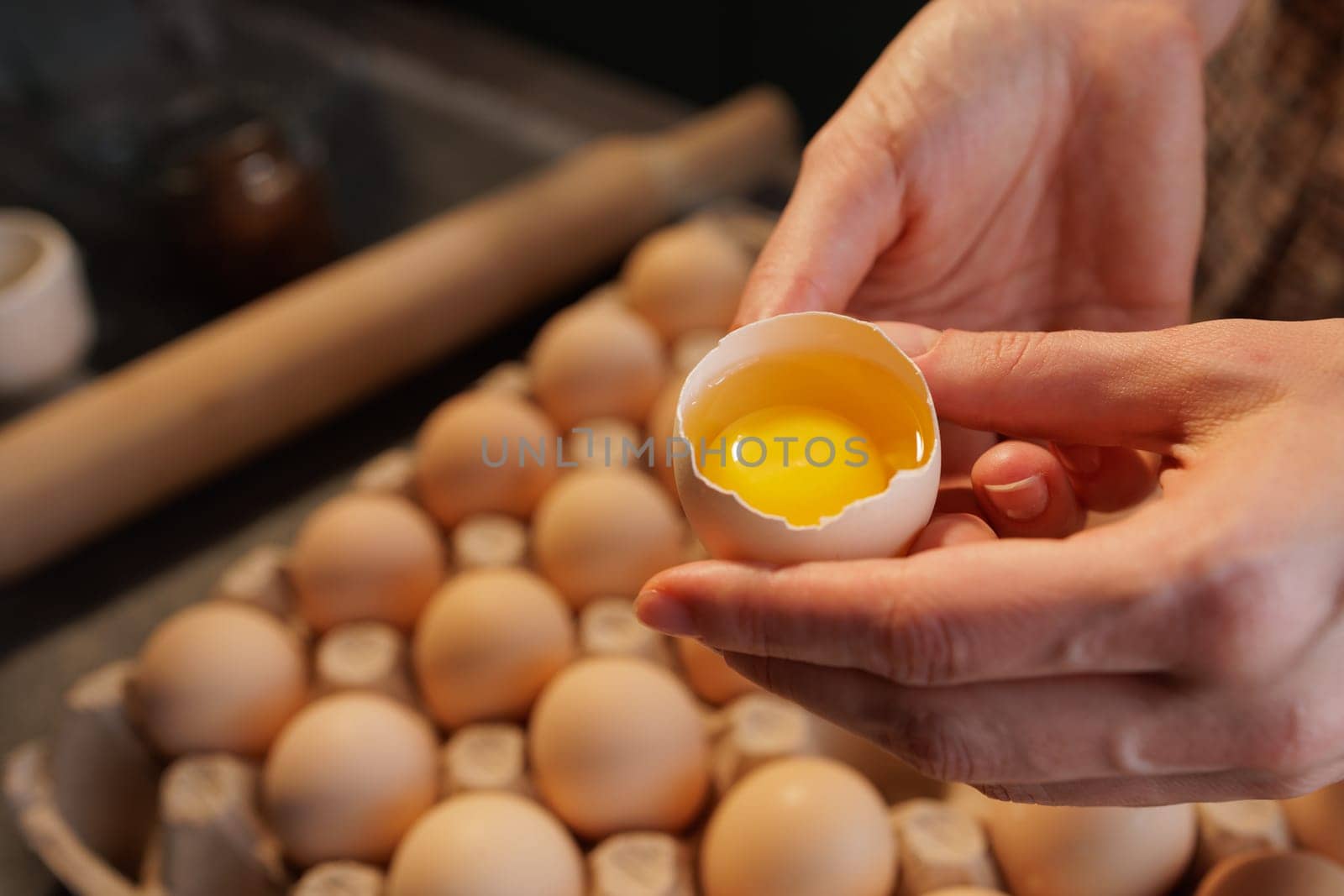 Close-up of female hands holding broken chicken egg on background of egg carton Close-up, healthy eating concept