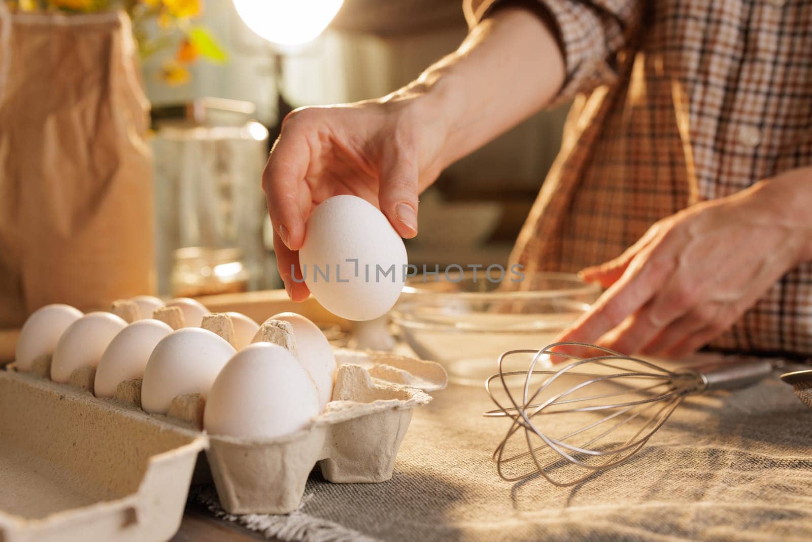 Hand taking chicken egg from box on kitchen table close-up against kitchen atmosphere