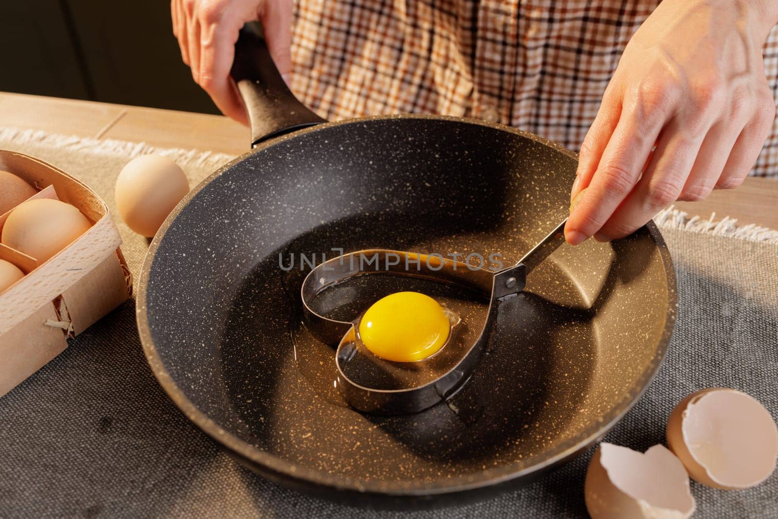 close-up of female hands holding a heart shape on a frying pan with a broken egg, heart-shaped fried egg