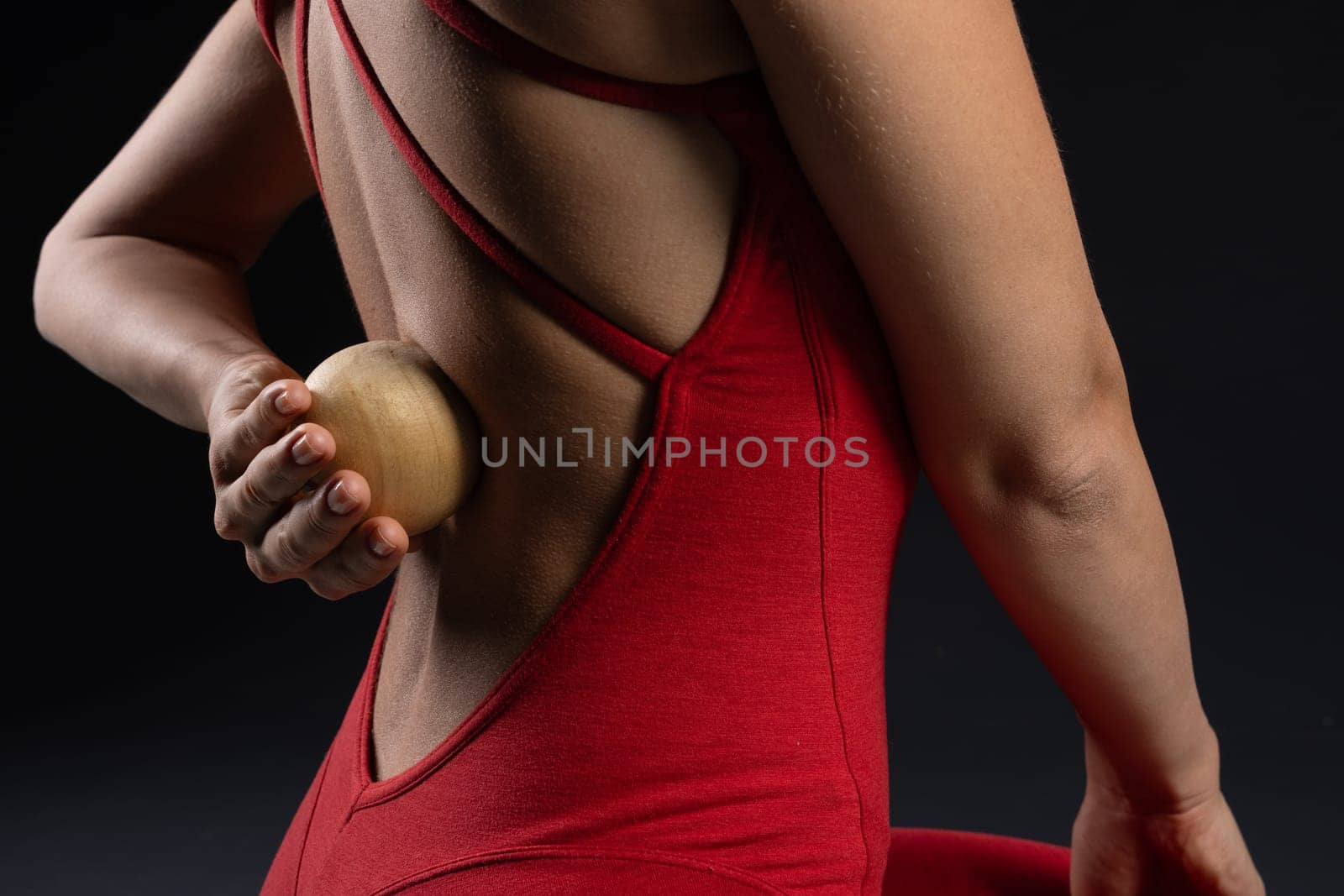 girl doing back muscle massage with wooden yoga ball in red t-shirt on dark background, self-care and relaxation techniques. self-massage tool