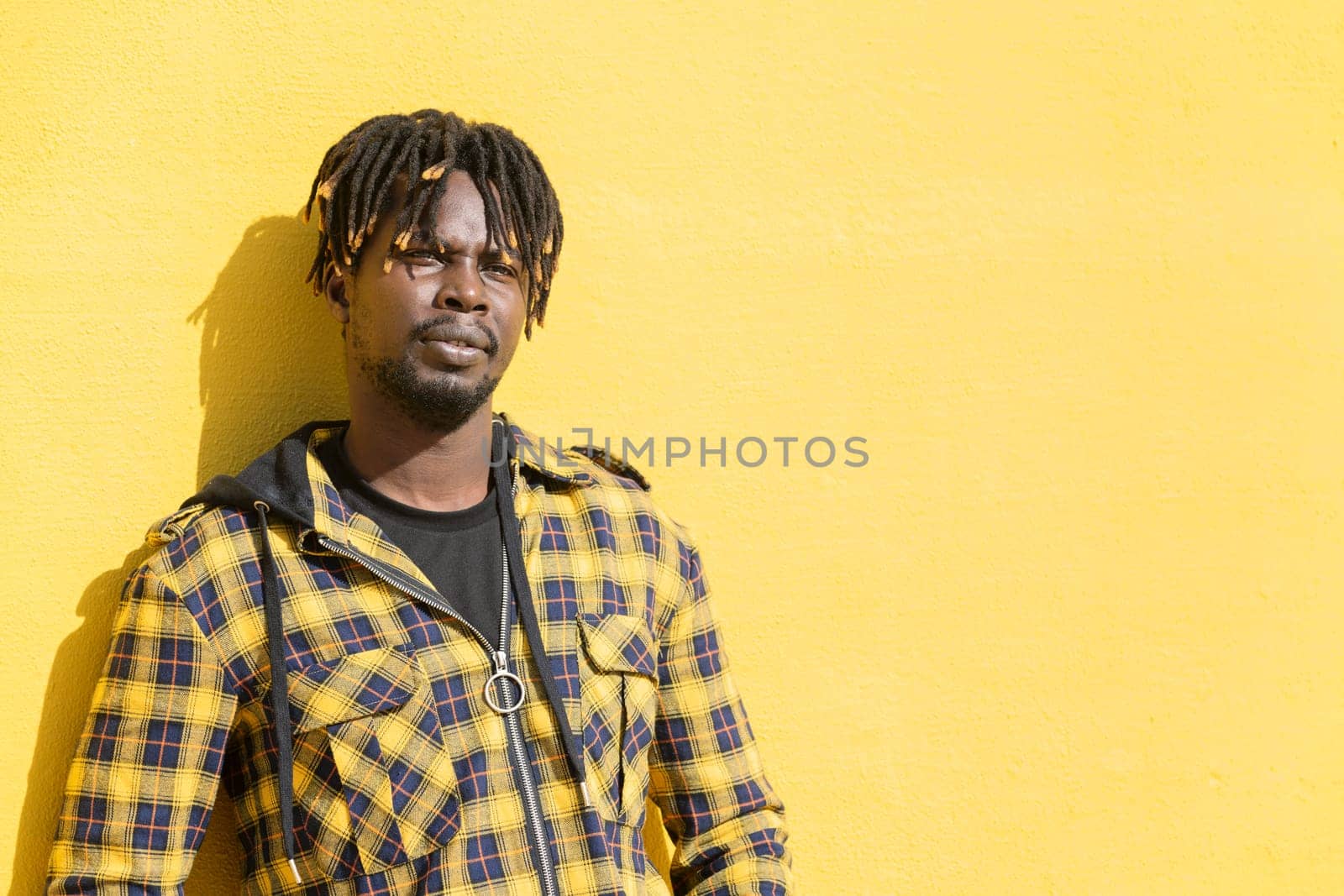 attractive young african man leaning against an intense yellow wall, lifestyle concept, copy space for text