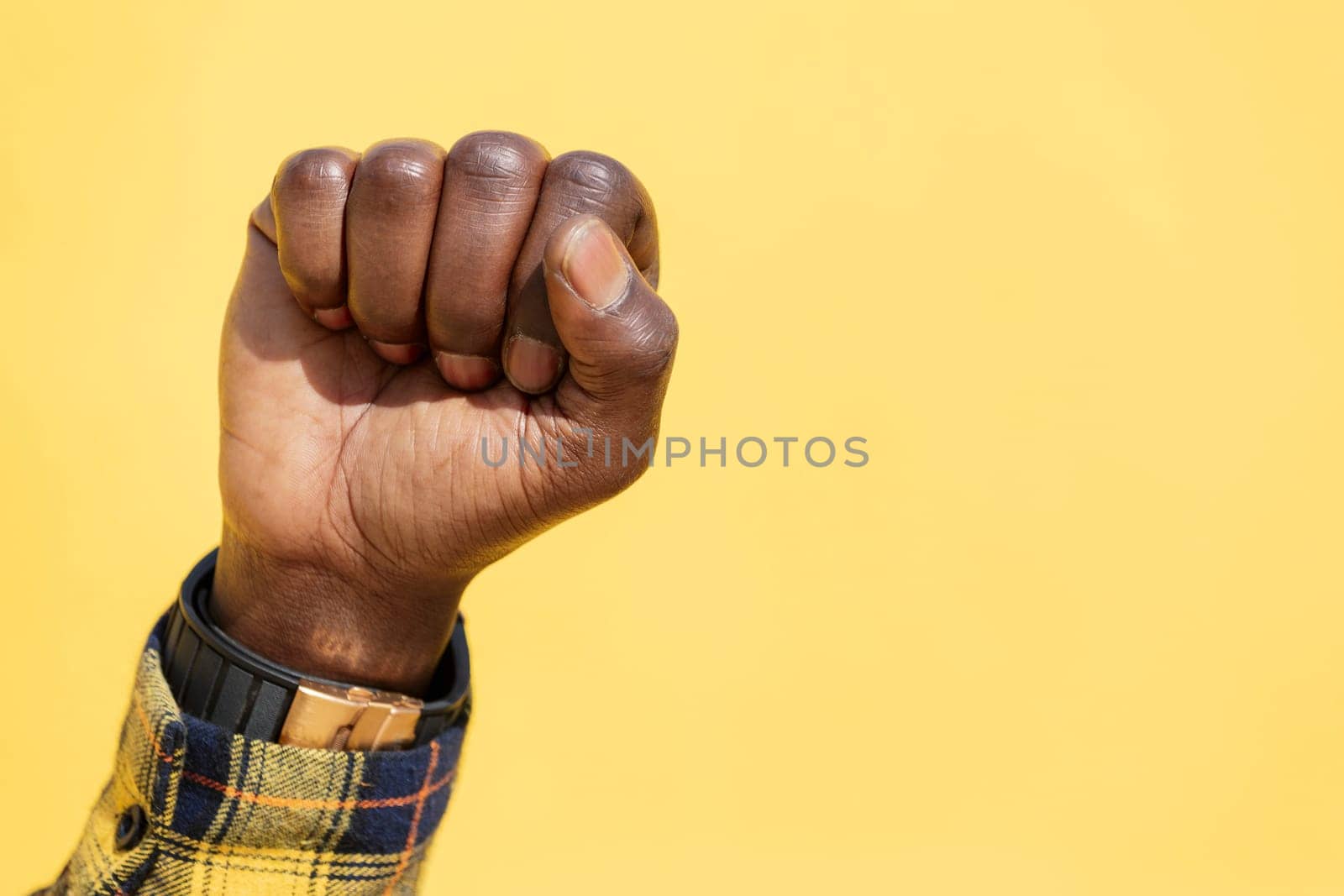 raised fist of a black man on an intense yellow background, concept of human rights struggle and lifestyle, copy space for text