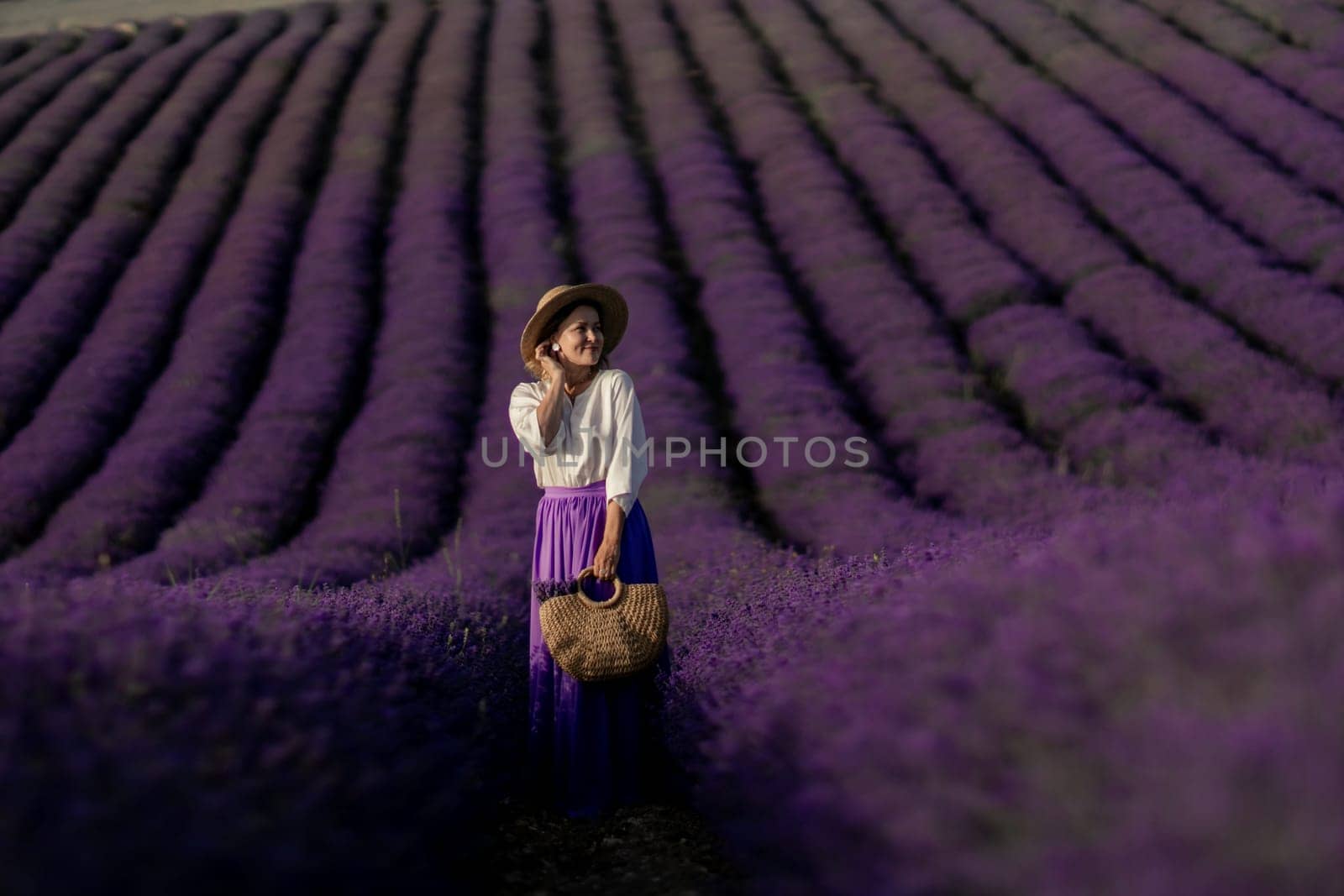 A woman stands in a field of lavender flowers. She is wearing a hat and a purple skirt