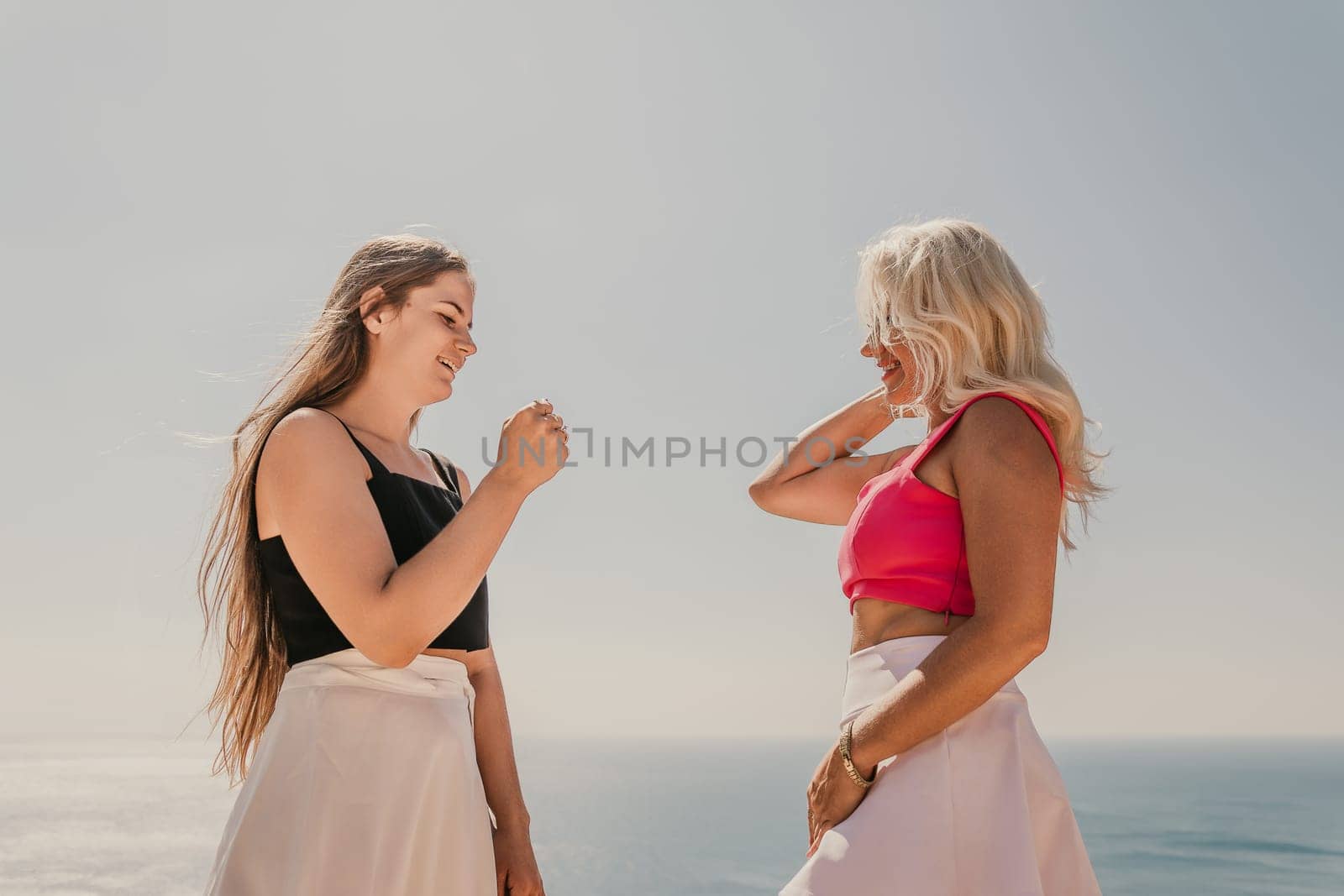 Two women shake hands on a beach. One is wearing a black tank top and the other is wearing a pink top