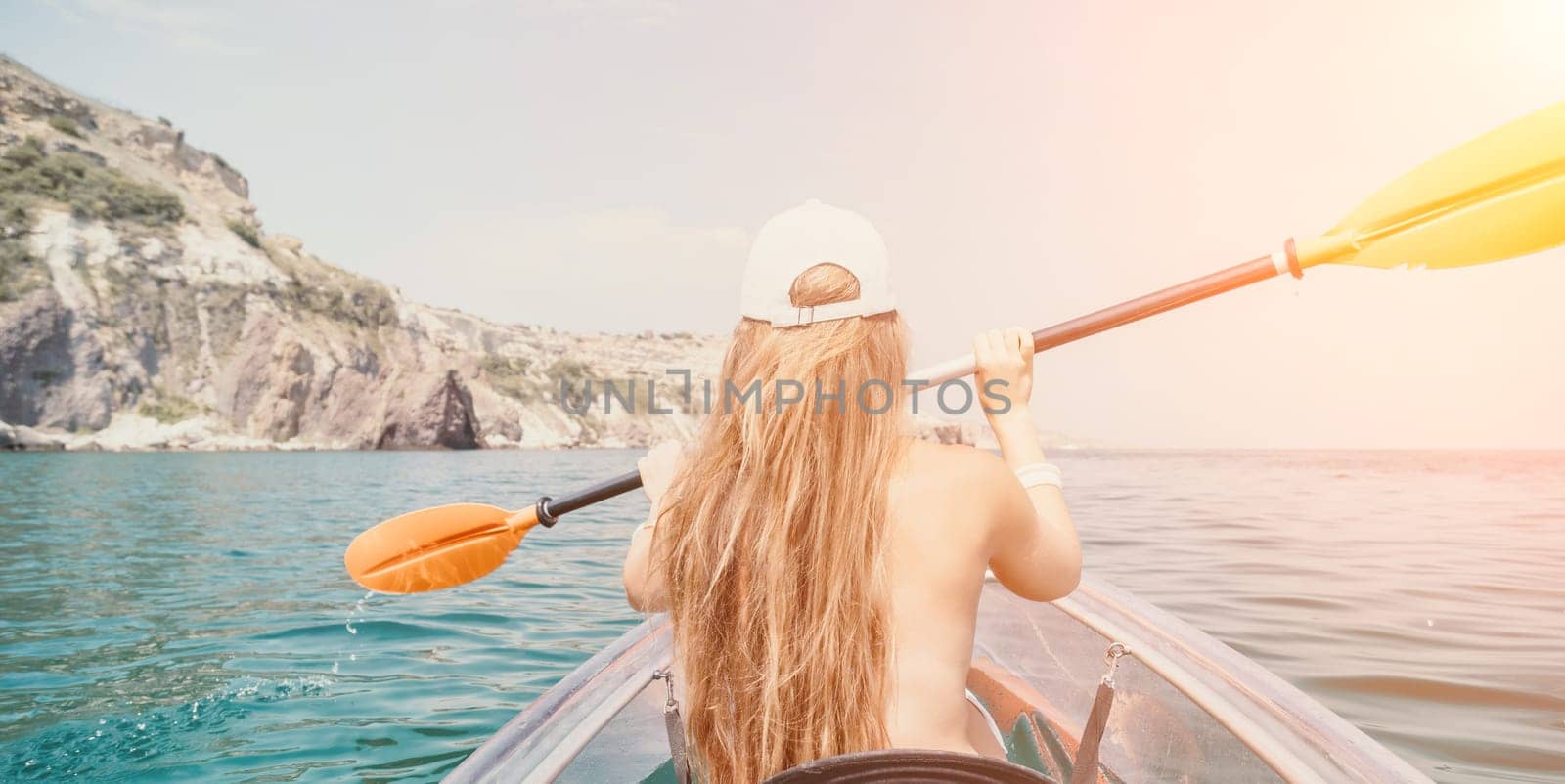 Woman in kayak back view. Happy young woman with long hair floating in transparent kayak on the crystal clear sea. Summer holiday vacation and cheerful female people having fun on the boat.