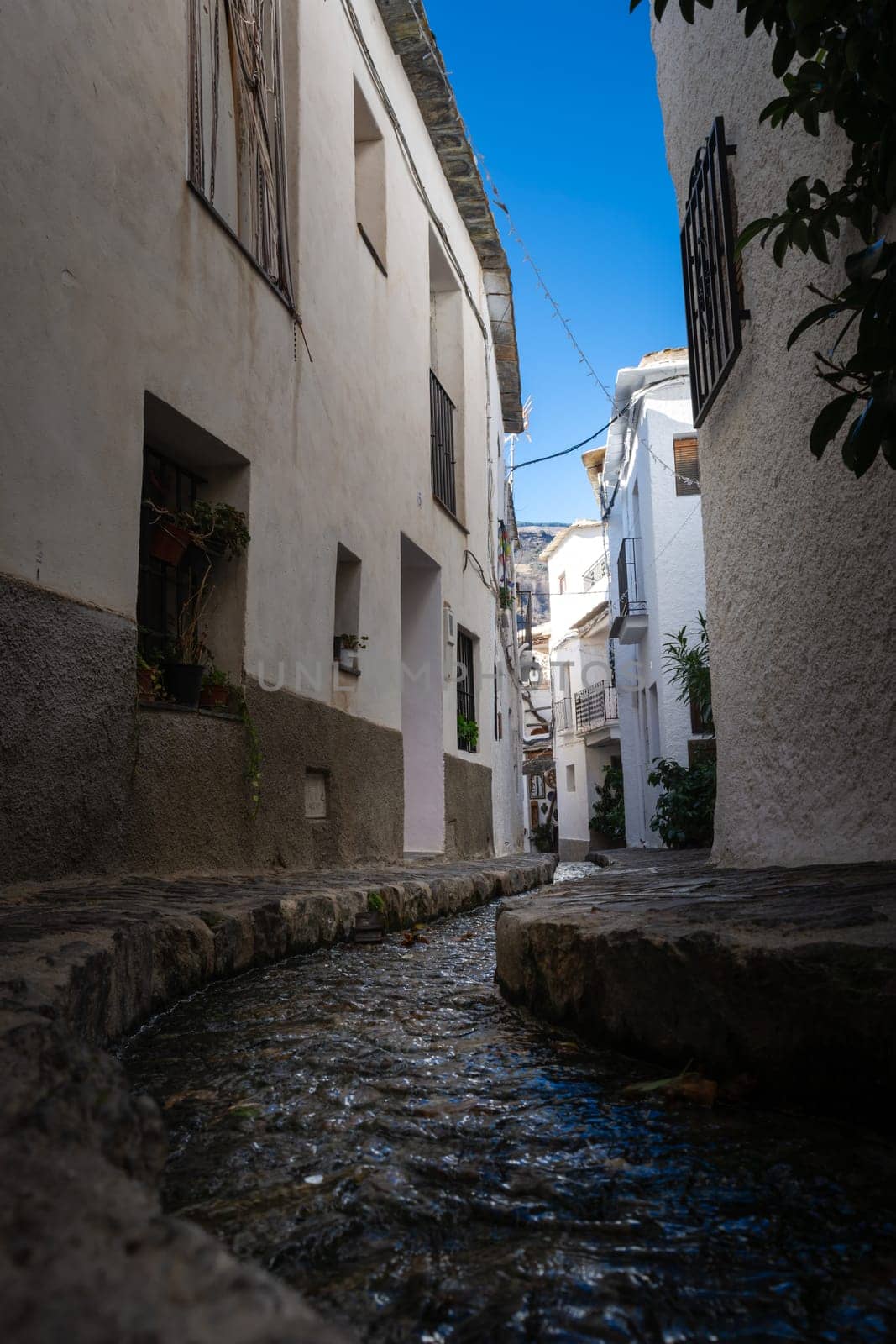 A small water stream flowing through a narrow alley of white buildings under a bright blue sky, Alpujarras, granada, andalucia, espa a,