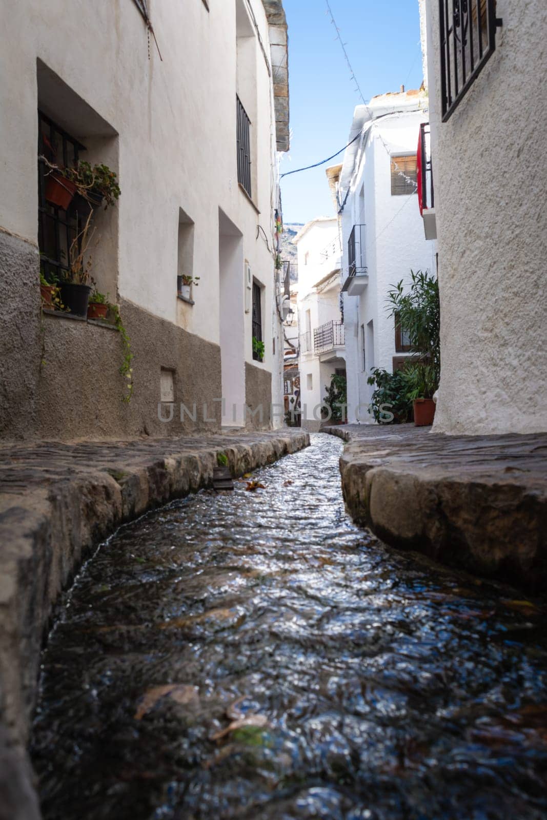 A narrow pathway with a small stream and white buildings on either side under a bright blue sky, Alpujarras, granada, andalucia, espa a,