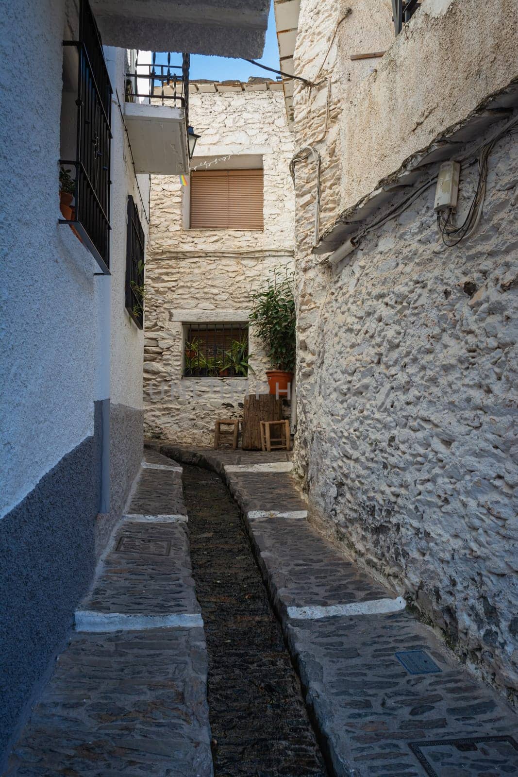 A small water stream flowing through a narrow alley of white buildings under a bright blue sky, Alpujarras, granada, andalucia, espa a,