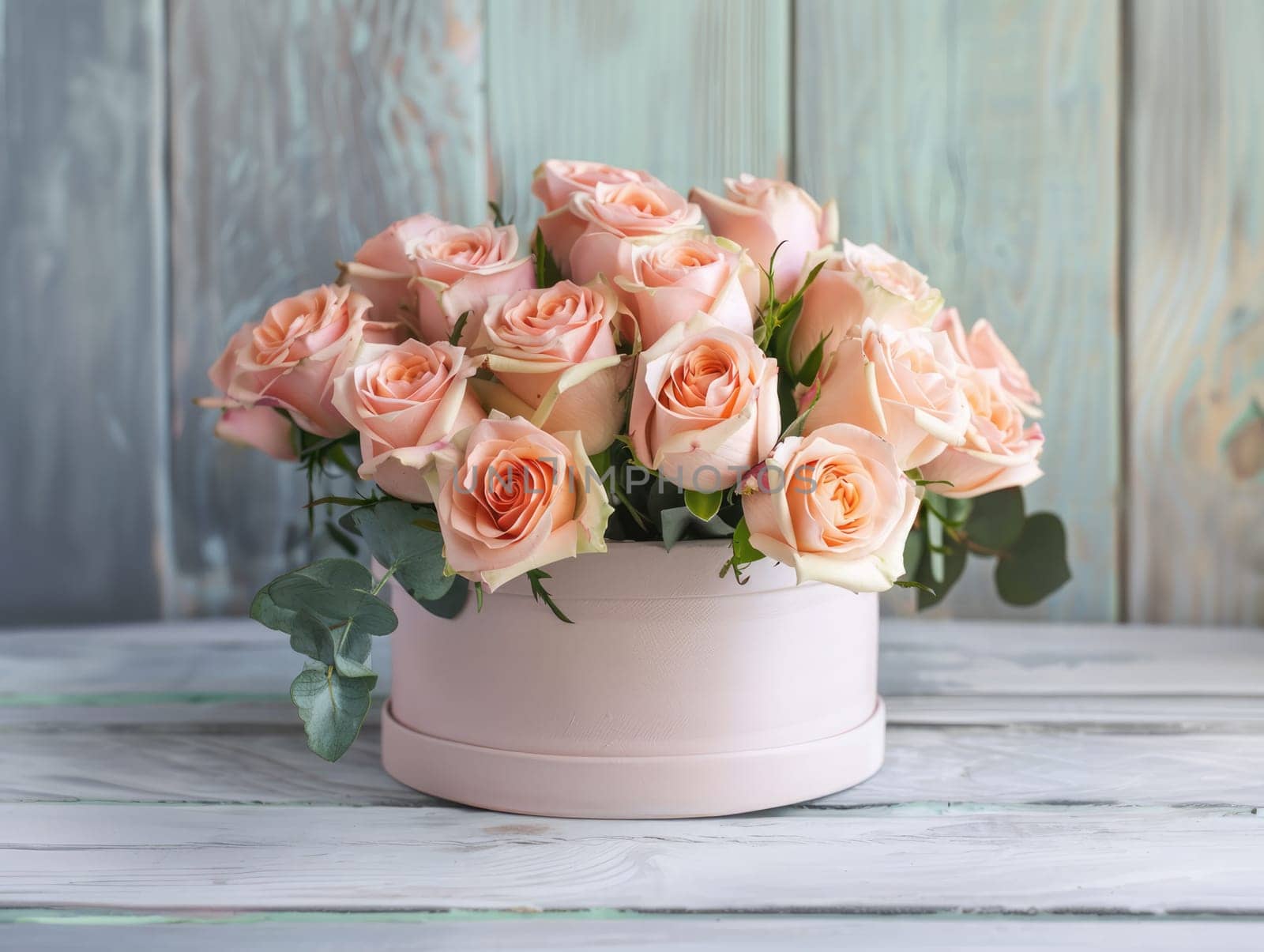 The delicate bouquet showcases vibrant pale pink roses surrounded by lush green leaves, elegantly placed in a soft pink container on a weathered wooden surface.