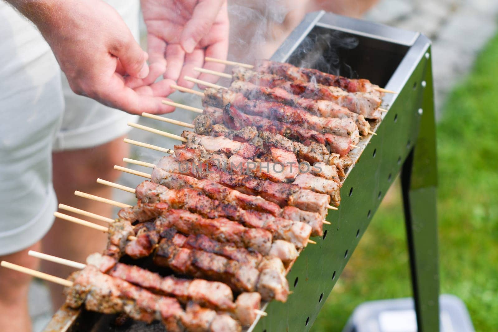young man grilling meat kebabs on coals, ARROSTICINI - typical southern Italian cuisine, a luxurious picnic on the terrace near the house in summer