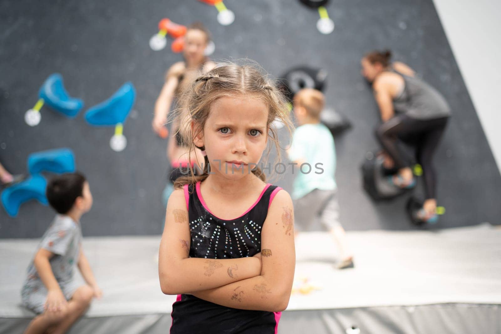 Portrait of confident little girl climber standing arms crossed in sports center. Female child looking at camera during rock climbing class. Essence of pursuing hobbies.