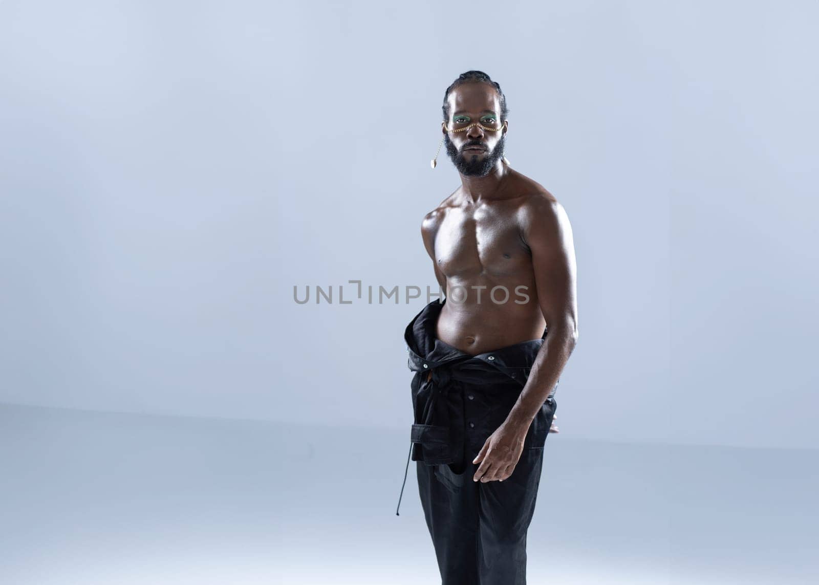 Confident shirtless African American gay man with bright makeup isolated on white background, Gay muscular macho man wearing make-up looking at camera.