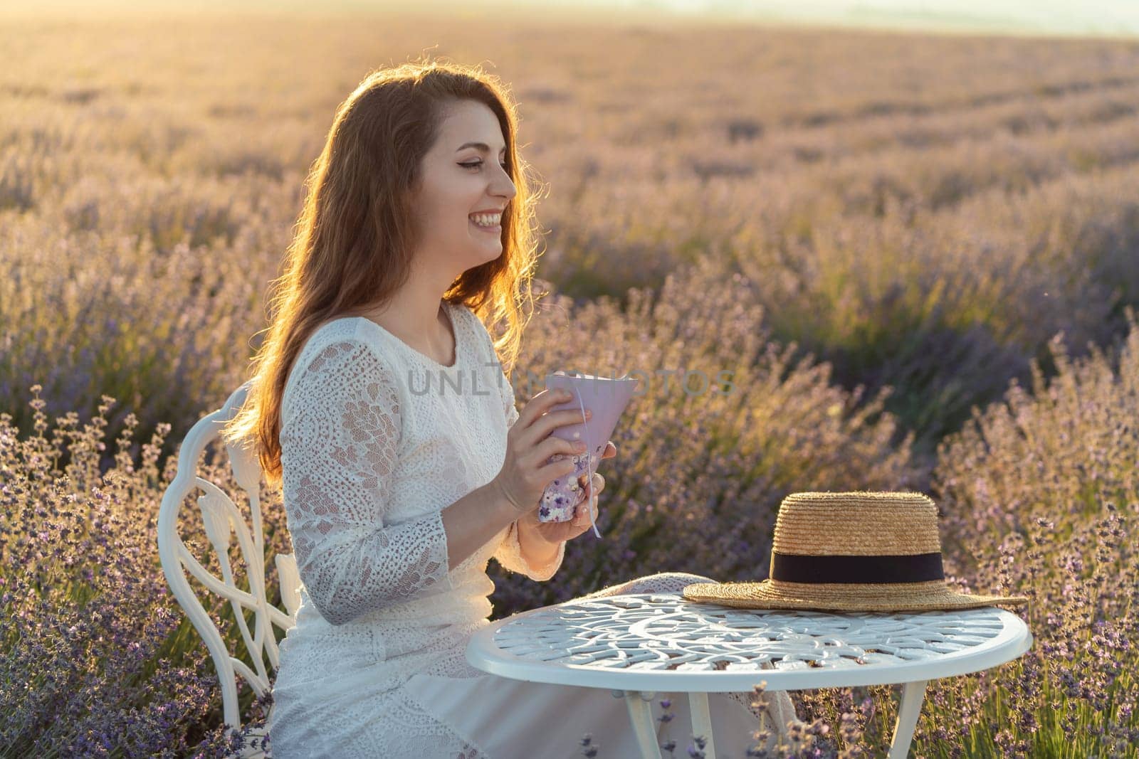 A woman is sitting in a field of lavender flowers, holding a book in her lap. She is in a peaceful and serene mood, possibly enjoying a quiet moment of reading or reflection