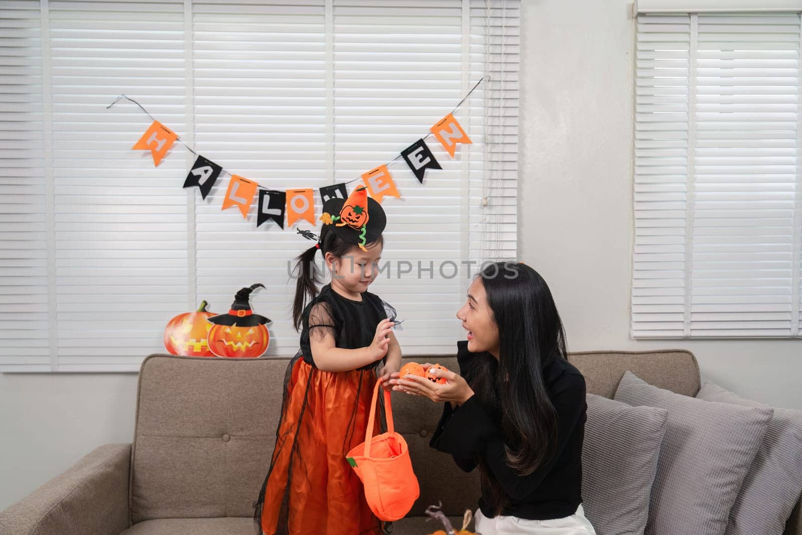 A mother and daughter enjoy Halloween festivities, surrounded by decorations and costumes, creating a warm and joyful family atmosphere.