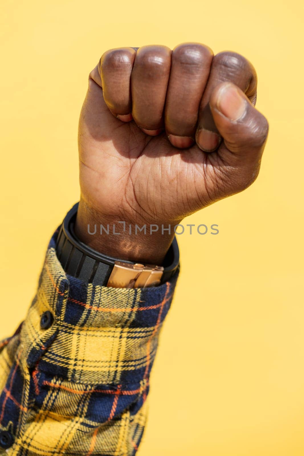 raised fist of a black man on an intense yellow background, concept of human rights struggle and lifestyle, copy space for text