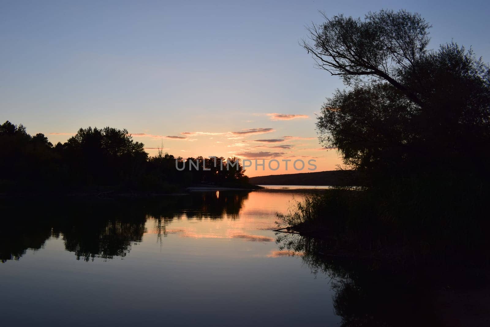 Majestic colorful sunset over forest lake in nature reserve. Beautiful lake in sunset lights. Scenic nature landscape. Bright sunset sky reflecting on the smooth water surface. Impressive sunsets.