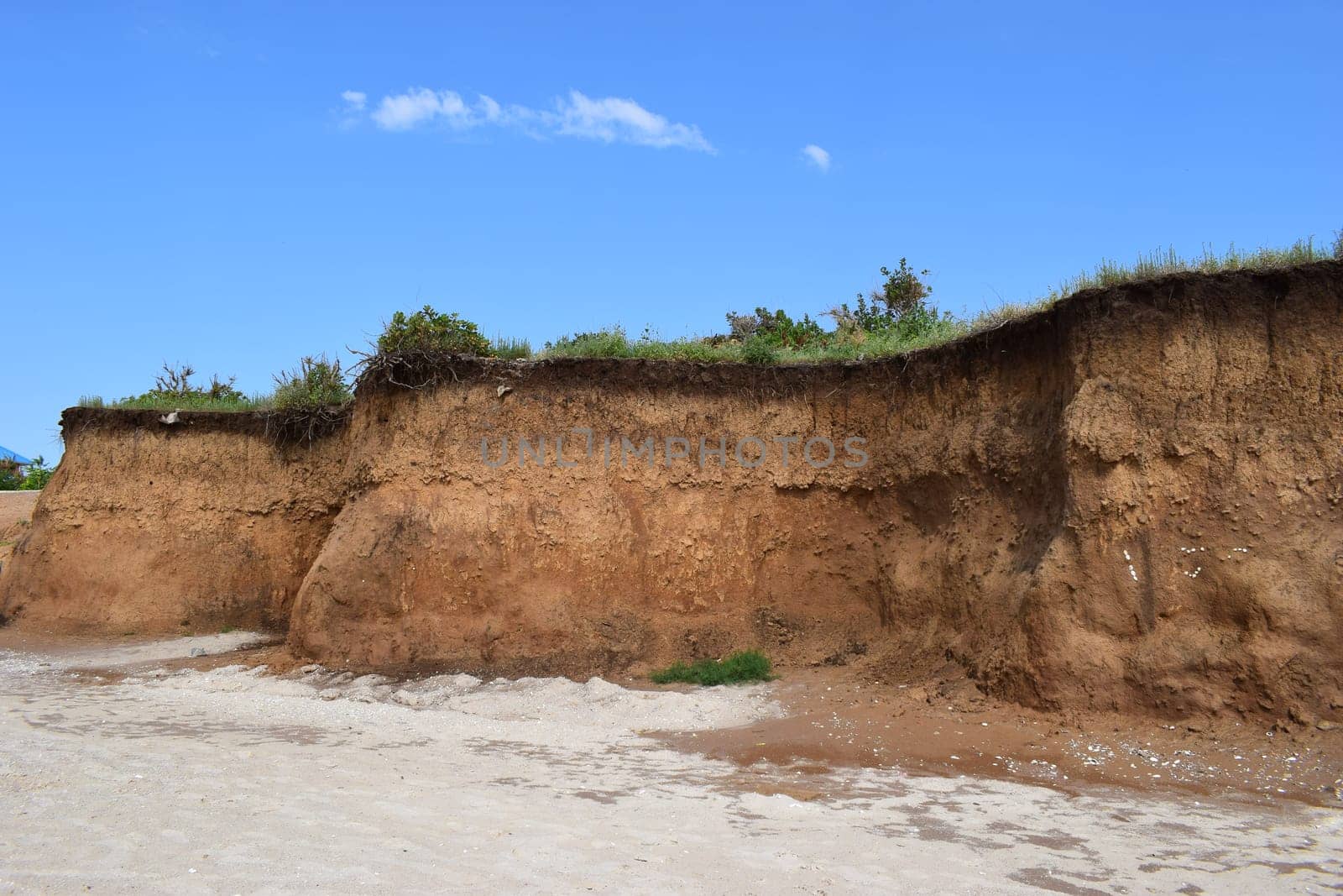 Sea cliffs of boulder clay in front of beaches. Clay Cliffs and Beach with Blue Sky and Water. Precipice coast near the sea. Visiting stunning sandy beach. Blue sky with huge red rocks and cliffs