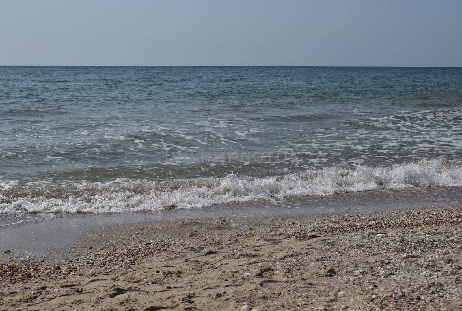 Beautiful landscape - turquoise colored sea water, sand, sky. The waves are on the sea to the shore. The Beach And Splashing Waves