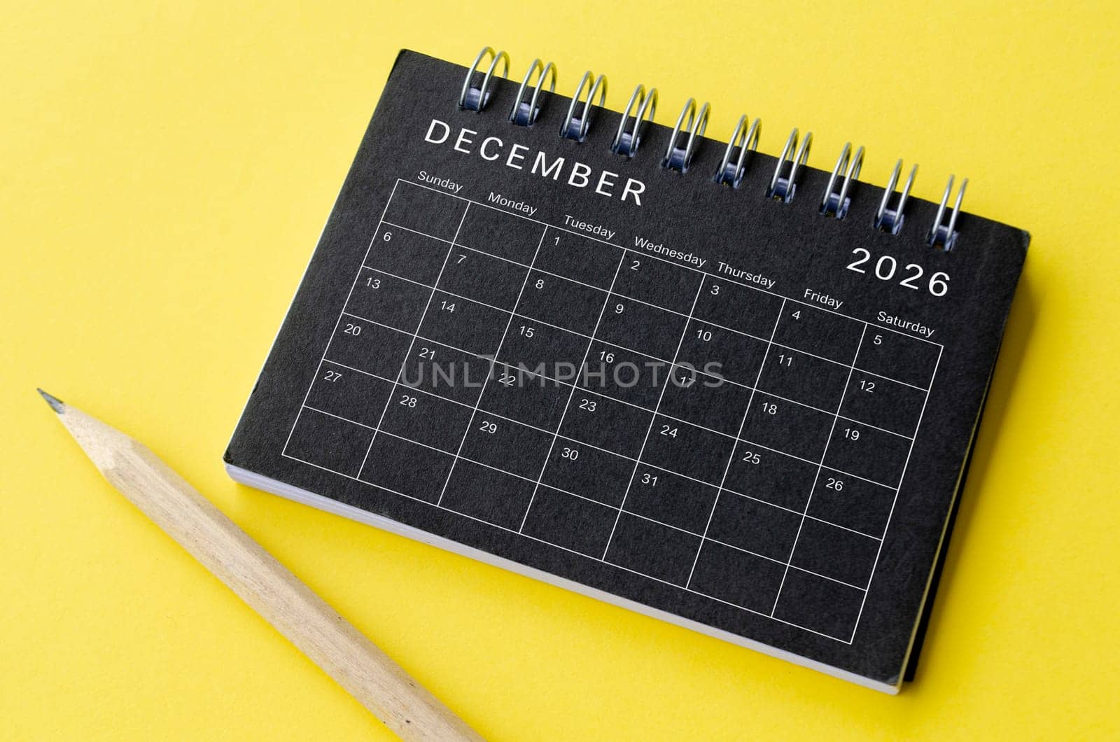 Top view of December 2026 calendar on black notepad with yellow background. Calendar concept.