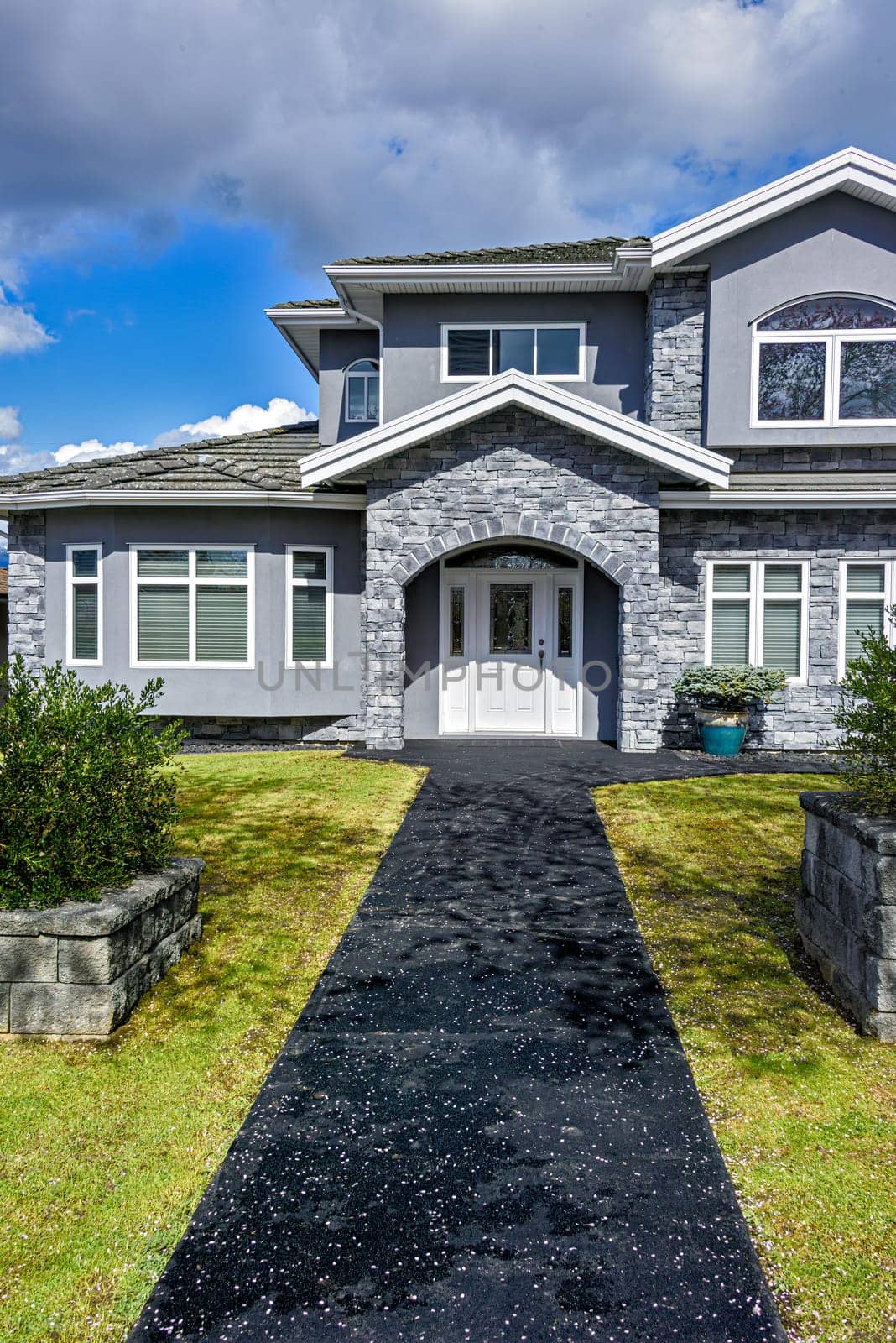 Nice residential house with stone texture walls and stone walls on front yard. Big family house with landscaped front yard