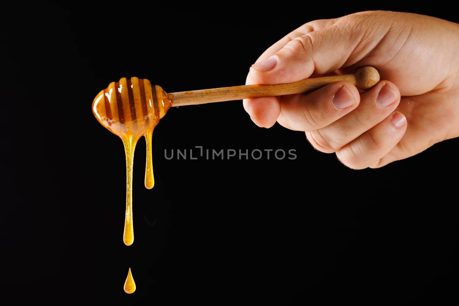 hand close up holding spoon with honey flowing and dripping on dark background, beekeeping concept, natural medicine