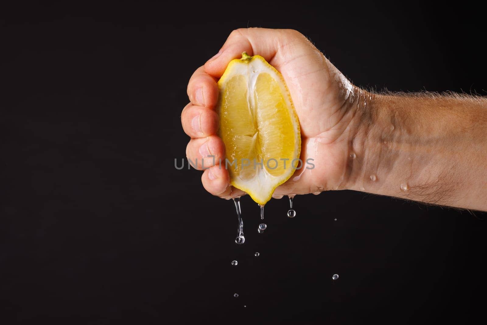 A hand squeezing a lemon, with juice dripping down. The background is black, highlighting the freshness of the lemon and the action of squeezing.