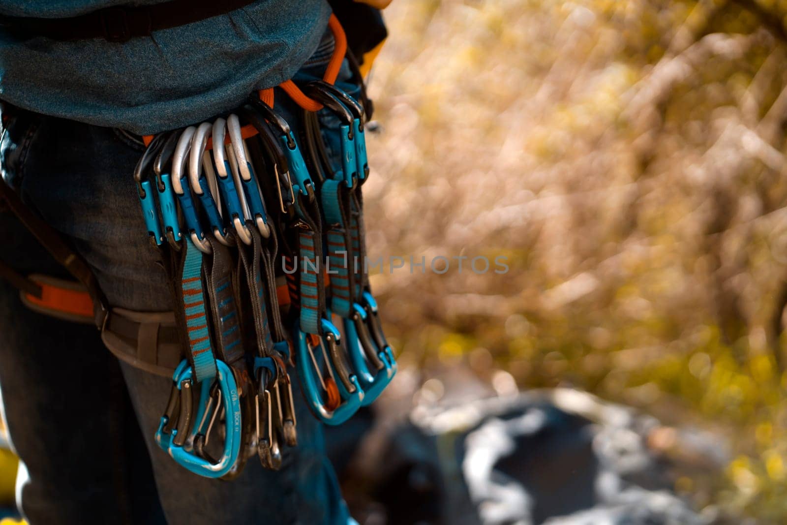 Young man, traveler is training outdoor with climbing equipment, safety belts, carabiners, rope, quickdraws close-up. Backpacker is involved in active sports, mountaineering and rock climbing.