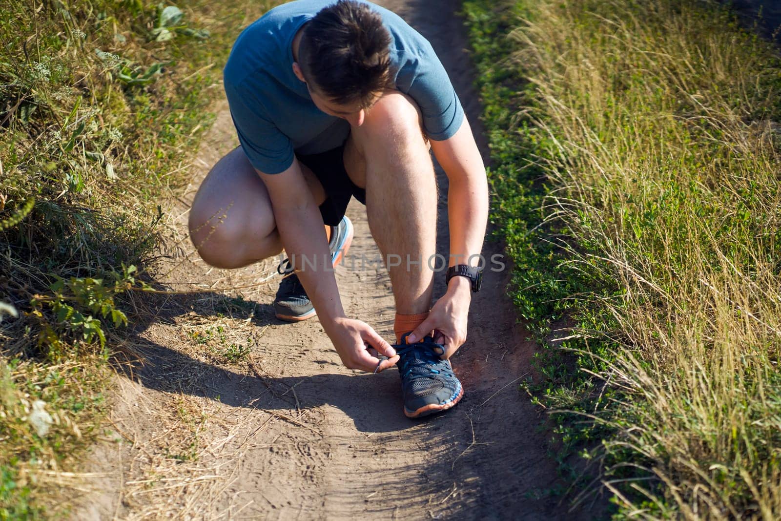 Close-up view of a young man tying his laces on his sneakers, getting ready for training and jogging along the trails in the park.