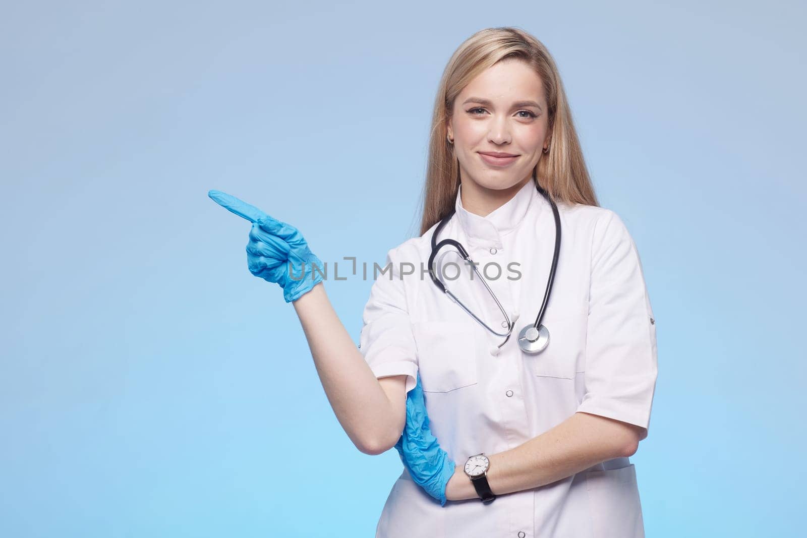 Beautiful lady doctor pointing with hand to copy space, studio shot. Isolated on blue background. Medical student, general practitioner.