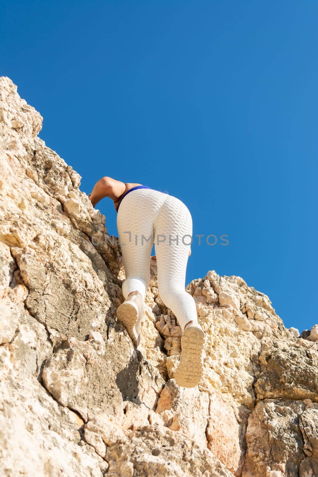 Woman climbing up the rock landscape, viewed from below, clear sky, Latin woman, middle-aged, outdoors, climbing psicobloc in mallorca, balearic islands, spain,
