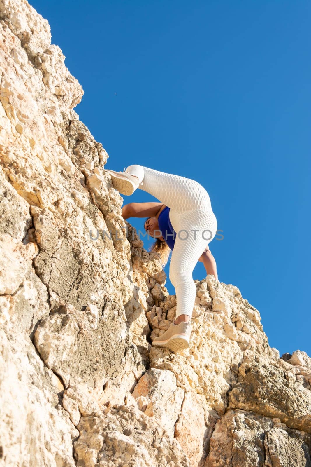 Woman in white leggings and blue top reaching higher on challenging rock terrain, Latin woman, middle-aged, outdoors, climbing psicobloc in mallorca, balearic islands, spain,