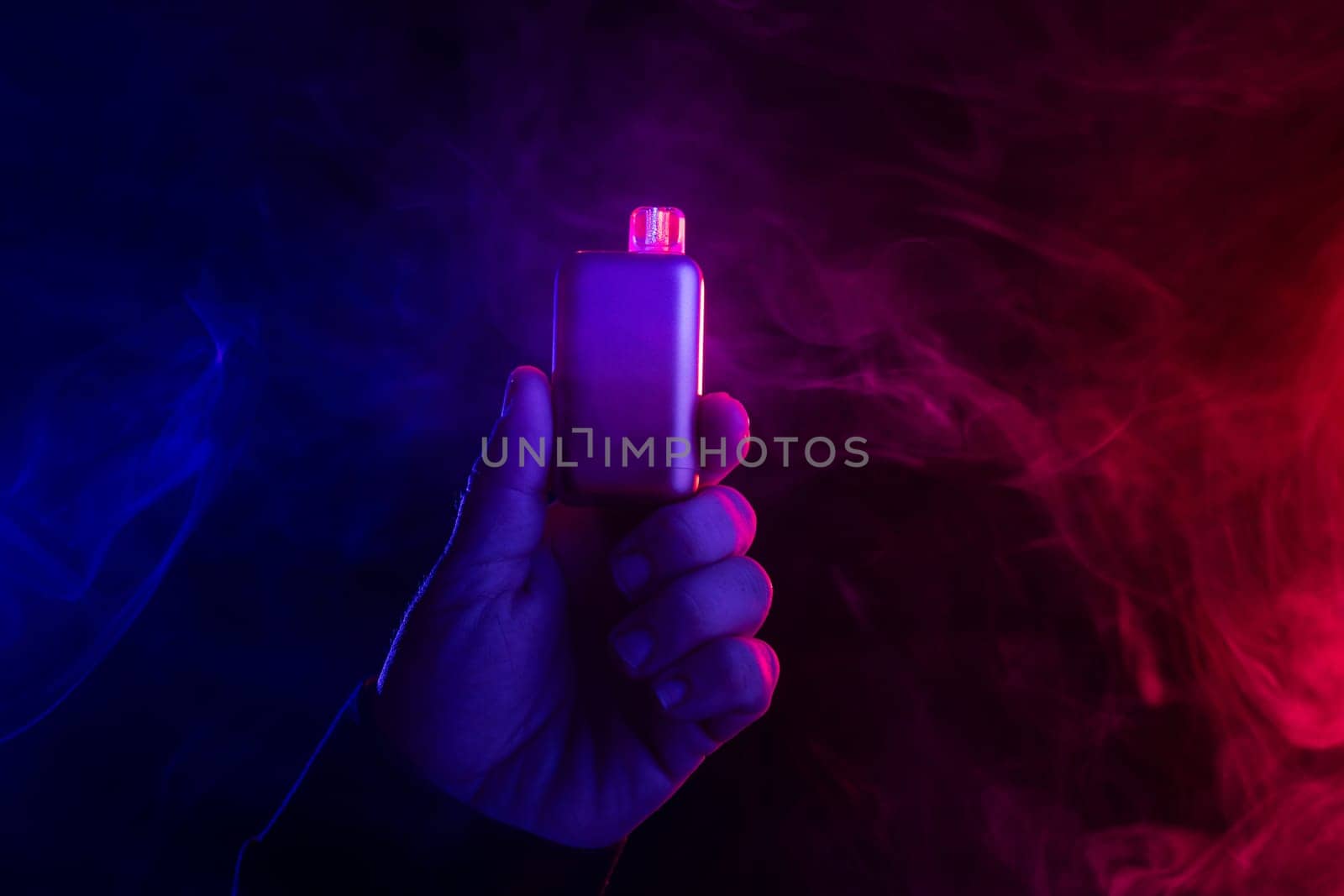 close-up hand holding vape electronic cigarette against colored smoke background, concept of harm of smoking