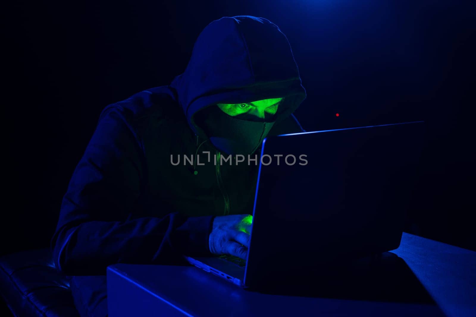 Cyber hacker in hood behind laptop in dark room, digital cyber security concept, computer hacking, information security