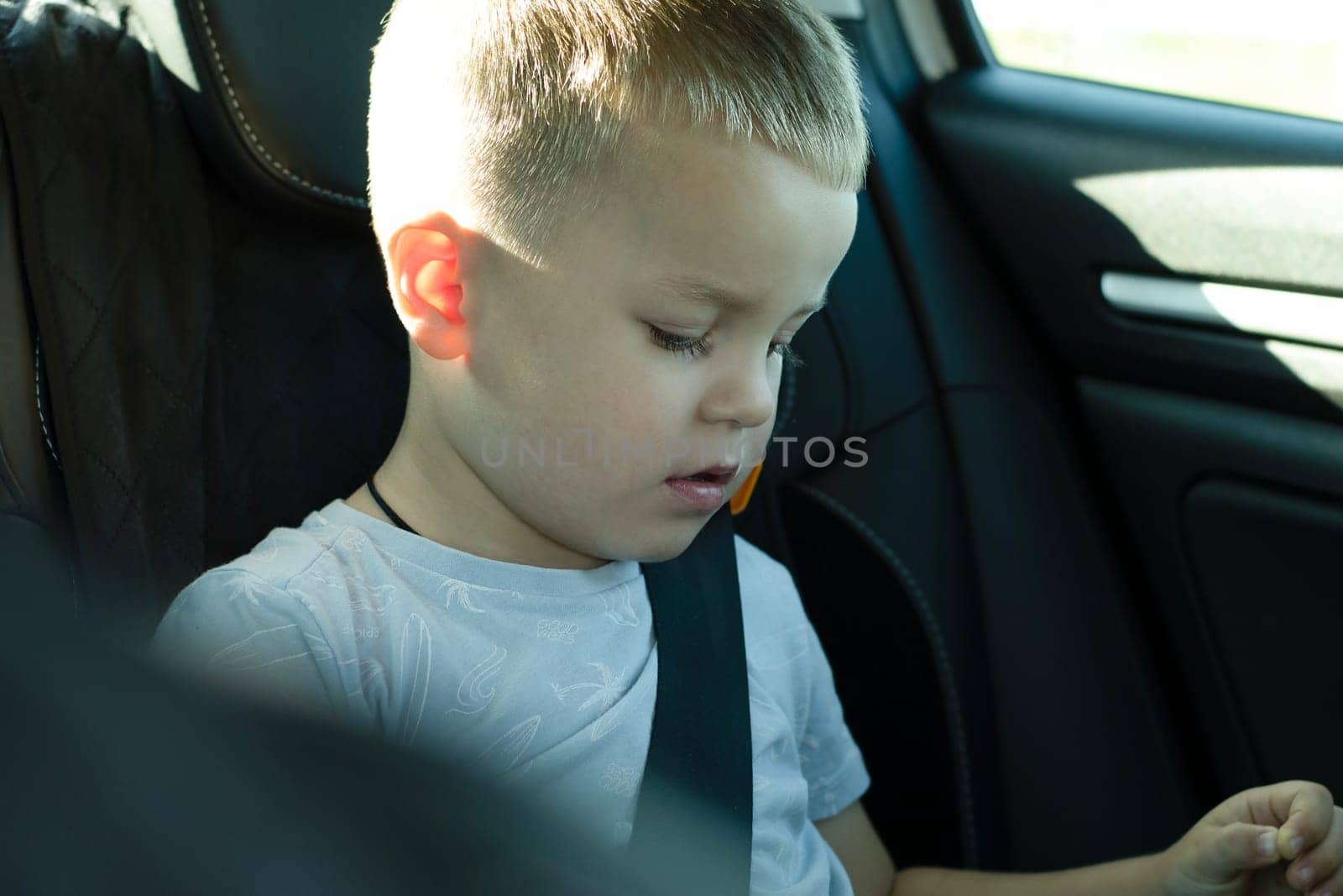 Security concept. A 4-year-old boy is riding in a car with a seat belt fastened in a child seat in the back seat. He travels with his family and watches cartoons on his iPad. Soft focus. Horizontal.