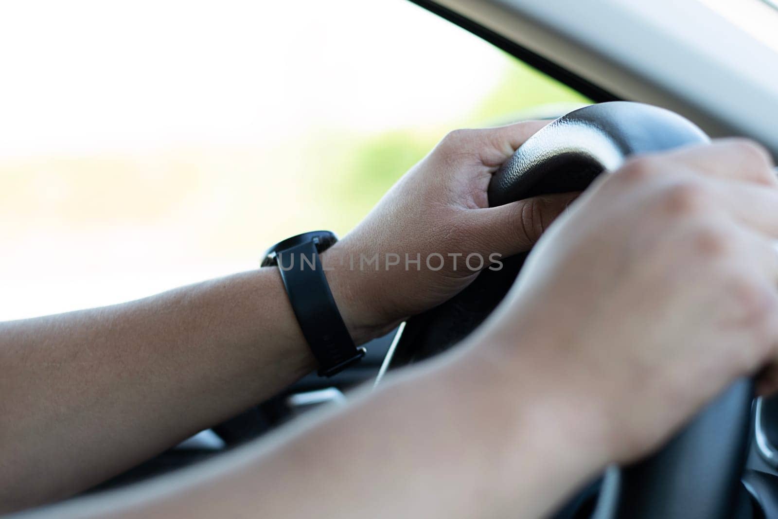 Auto concept. Male hands firmly hold the black steering wheel of a car. The driver moves on the highway during the day. Close-up. Soft focus.