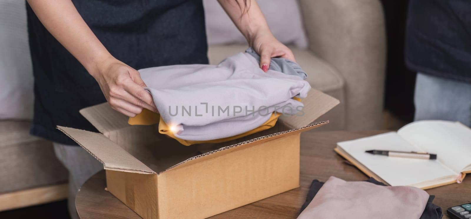 Close-up shot of a young woman packing a shirt into a box to deliver the product to a customer. by wichayada