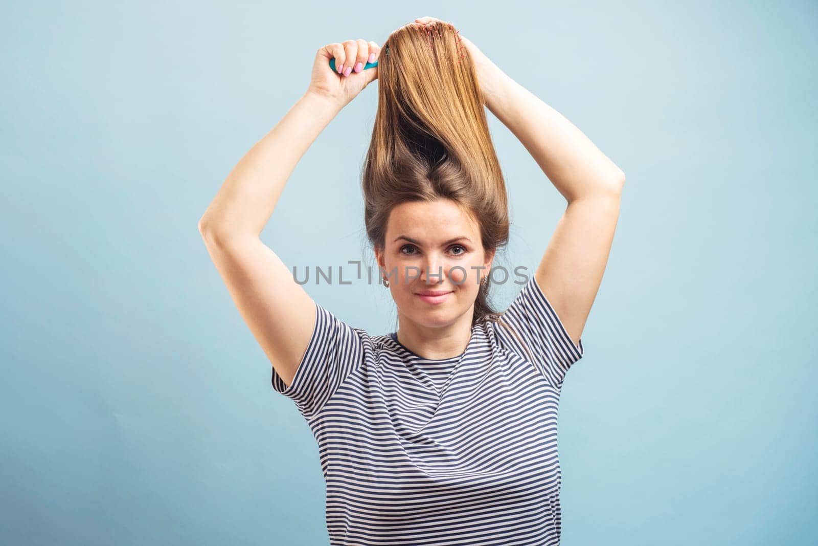 Beautiful brown-haired woman brushing her beautiful shiny hair with hairbrush on blue background